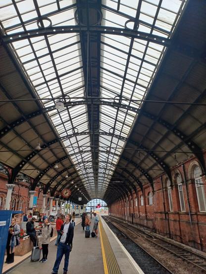 the victorian architecture station domed roof with a skylight all along the centre above the rail track on the right & the platform in the middle.