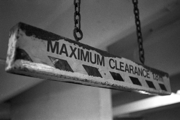 Hanging from two rusted chains, a battered wooden bar reads “maximum clearance 1.8m”.