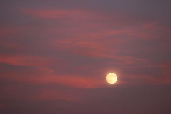 Photo of a nearly full moon surrounded by pink clouds.