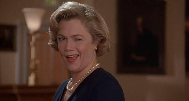 A manicured blonde white woman with a string of pearls winks saucily