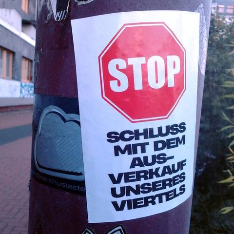 Aufkleber auf einem Laternenmast in Linden/Nord: Bild eines Stoppschildes, darunter der Text »Schluss mit dem Ausverkauf unseres Viertels«.