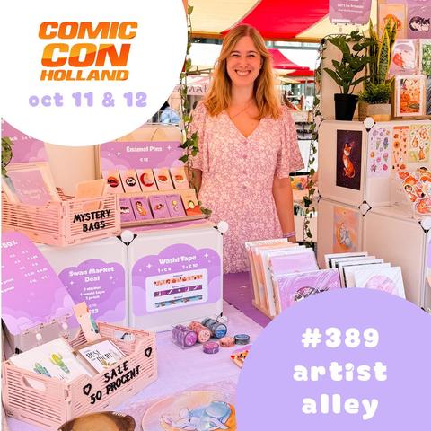 A photo of a blond woman called Leonie behind her purple booth filled with cute stationery, enamel pins and artwork.