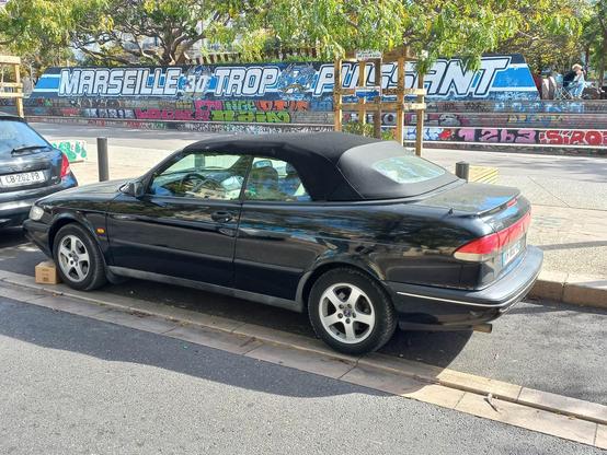 A parked black convertible car, with black soft top, seen from the rear.