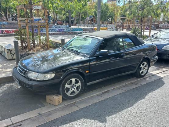 A parked black convertible car, with black soft top, seen from the front.