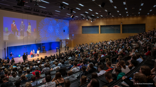 Foto vom Audimax der TU Dresden. Der Hörsaal ist voll. Vor dem Publikum sitzen Personen in einer Gesprächsrunde.