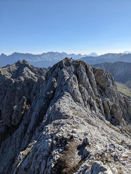 In the front smaller mountains and a small cross, in the back more mountain summits in clear blue sky