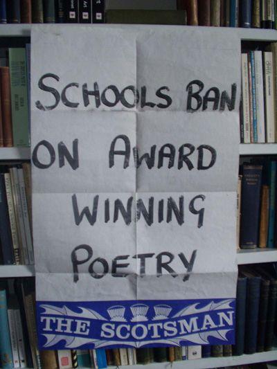 A sheet of paper from a newspaper hoarding, suspended in front of a set of bookshelves. The paper hoarding is creased, having been folded up for a long time. The hoarding is white, with a blue bar along the bottom bearing the logo of THE SCOTSMAN newspaper. The headline is hand-written in thick black marker pen:

SCHOOLS BAN
ON AWARD
WINNING
POETRY