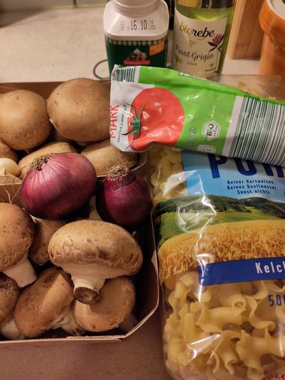 Die Zutaten für das Gericht, darunter braune Champignons, Zwiebel, Knoblauch Weißwein, Kochsahne und Nudeln