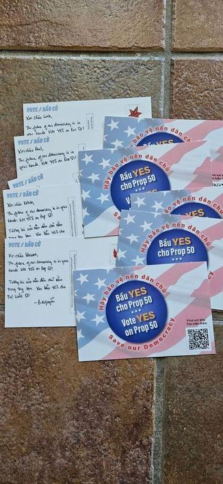 Postcards with the American flag in red, white, and blue graphic features a blue circle with the message "Vote YES on Prop 50" in English and Vietnamese on one side. On the plain side, there are handwritten messages: "Xin chào [Voter’s First Name], 

The future of our democracy is in your hands.Vote YES on Prop 50!

Tương lai của nền dân chủ nằm trong tay bạn. Xin bầu YES cho Dự Luật 50!"

- [Your First Name]