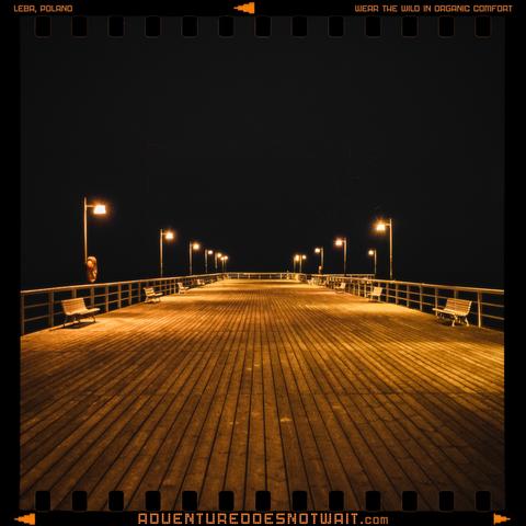 A wooden pier in Łeba, Poland, lit by street lamps at night, inspiring sustainable hoodies for organic comfort in the wild.