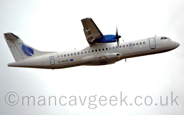 Side view of a white, high-winged, twin propellor-engined airliner flying from left to right at a very low altitude, with undercarriage already retracted, flaps extended from the rear of the wings, and the nose raised, suggesting it has just taken off.
The plane is almost entirely white, with a grey belly, and vivid blue engine pods mounted on the front of the wings.
The black registration "EI-REH" is on the lower rear fuselage, next to small Irish and EU flags.
A blue feather with a grey drop shadow is in the middle of the white tail.
Bright but hazy sky with hints of blue on the sides fills the rest of the frame.