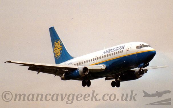 Side view of a twin-engined jet airliner flying from left to right at a low altitude, with undercarriage lowered and flaps extended from the rear of the wings, suggesting it is about to land.
The plane is largely white, with a blue lower fuselage with a thin yellow stripe separating the 2 colours, and dark blue "Ambassador" titles on the upper forward fuselage.
The black registration "G-BVFB" is on the upper rear fuselage.
The tail is blue, with the yellow outline of a circle, containing 6 letter "A"'s, arranged in a circle, all connected by their topmost point.
The engine pods mounted under the wings are also blue.
Flat grey sky fills the rest of the frame.