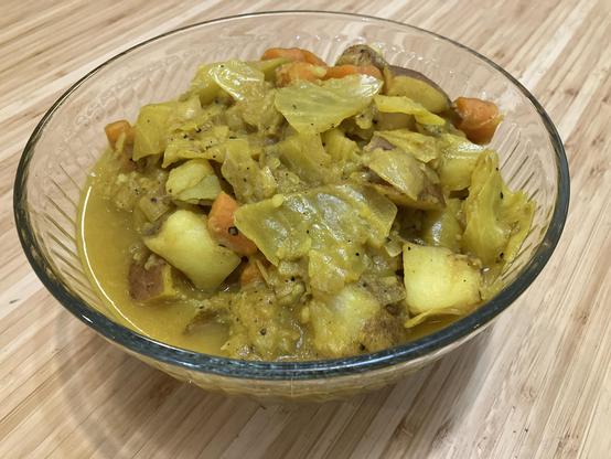 A turmeric-coloured vegetable stew with cabbage, carrots, potatoes, and onions in a large glass bowl.