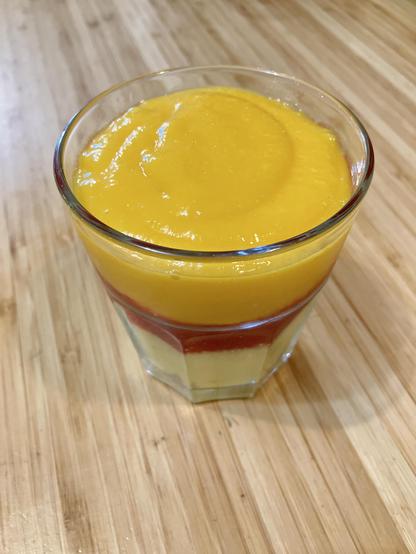 A glass with layers of yellow, red, and orange pureed fruit.
