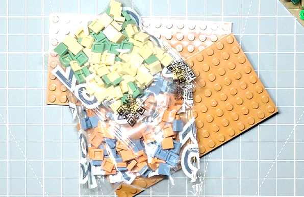 Two bags of probably a hundred Lego one-by-one tiles in four colors, thrown on top of two large orange Lego plates.