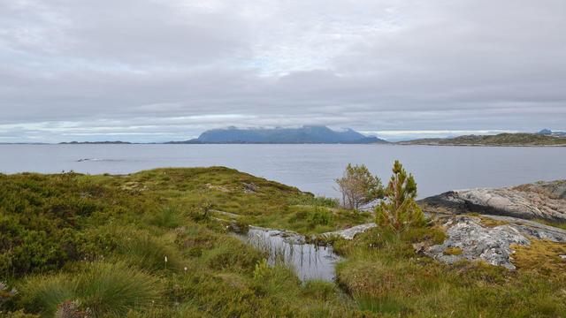 A photo looking out over a large body of water toward a mountainous island. The sky is filled with clouds.