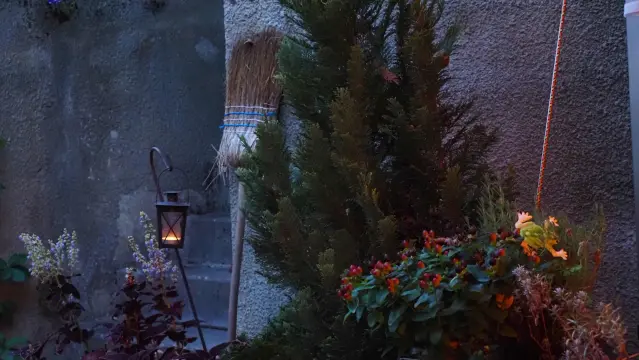 Besen steht an einer Mauer, eine kleine Lampe mit Kerze brennt