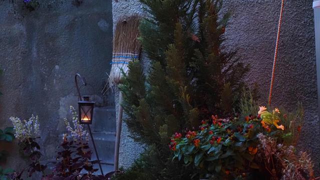 Besen steht an einer Mauer, eine kleine Lampe mit Kerze brennt