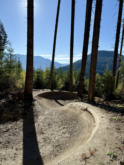 A swooping pair of large smooth bermed turns on a forest singletrack with mountains in the background