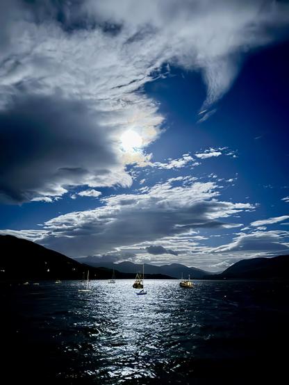 Boats moored in a harbour under a full moon with a few moonlit clouds.