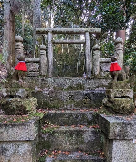 Moss covered stone steps leading to Astone torii with stone foxes wearing red bibs either side.