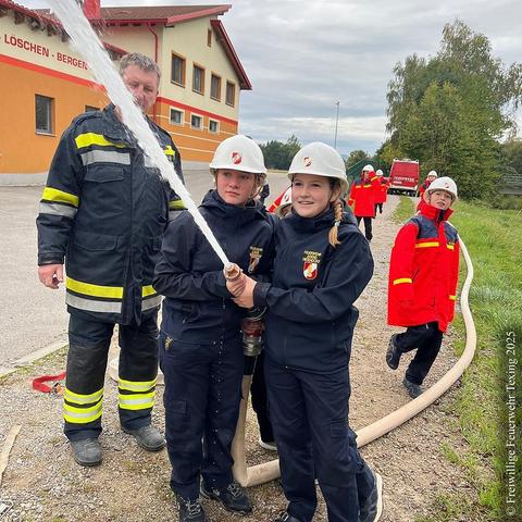 Zwei Mitglieder der Feuerwehrjugend der freiwilligen Feuerwehr Diesendorf stehen gemeinsam an einem Strahlrohr und spritzen. 

Links daneben steht ein Feuerwehrmann der freiwilligen Feuerwehr Diesendorf als Aufsicht, im Hintergrund sieht man ein Kleinlöschfahrzeug und mehrere Mitglieder der Feuerwehrjugend Texing-St. Gotthard bekleidet in roten Einsatzjacken und mit weißen Schutzhelmen. 

English:
Two members of the volunteer fire department’s youth brigade in Diesendorf stand together at a water‑stream nozzle, spraying water.

To the left stands a volunteer firefighter from Diesendorf acting as supervisor; in the background a small fire‑engine can be seen along with several members of the Texing‑St. Gotthard youth fire brigade dressed in red duty jackets and white protective helmets.