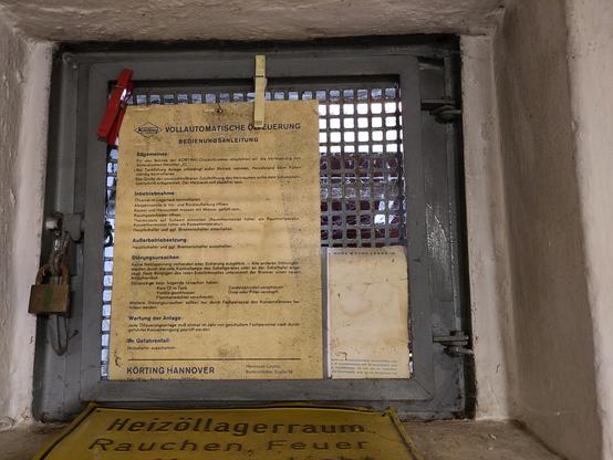 Ein Altbau Kellerfenster mit Metallgitter. In der Fassung vor dem Gitter fehlt die Glasscheibe.