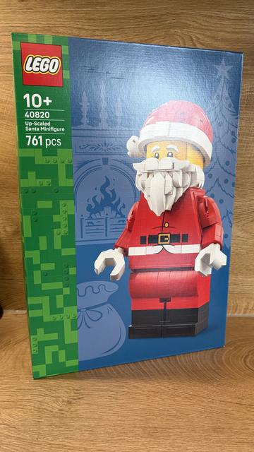 Dies ist das Cover einer Lego-Verpackungsbox. Die Box ist hauptsächlich grün, mit einem Pixelmuster auf der linken Seite und einem blauen Hintergrund mit Schneeflocken. Das Hauptbild ist eine Lego-Figur des Weihnachtsmanns, die das meiste Zentrum der Box einnimmt. Der Weihnachtsmann ist rot und weiß und trägt einen Gürtel. In der linken oberen Ecke steht „LEGO“ in weißen Buchstaben. Auf der linken Seite befindet sich ein Feld mit der Aufschrift „10+ 40820 Up-Scaled Santa Minifigure 761 pcs“.