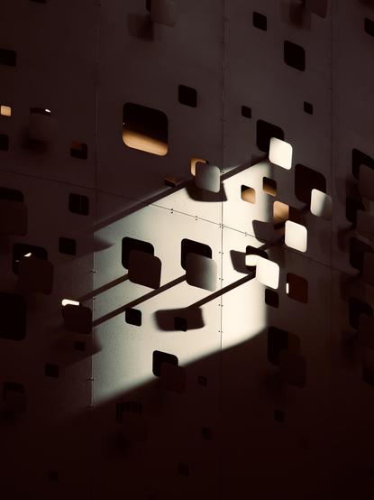 A close-up of a metal structure with square pieces cut out of it and placed forward compared to the main structure. Light shining diagonally on it makes the metal and shadows play in interesting ways, creating structures that weren't there before.