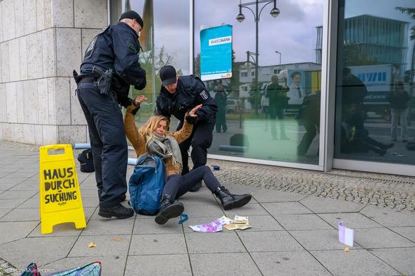 Neue Generation macht Hausdurchsuchung im Konrad-Adenauer-Haus wegen Verdacht auf Korruption. Polizei verhaftet Aktivistin. Warnschild mit „Hausdurchsuchung“. Am Haus klebt ein Plakat der Neuen Generation mit „#Merzmafia/Rückkehr der #Klimakleber“. Auf dem Boden sind Geldscheine verstreut. Berlin, 06.10.2025