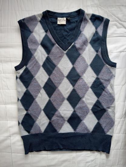 Ein Pullunder mit einem dunkelblauen, hellblauen Rautenmuster. Der Pullunder hat einen V-Ausschnitt und liegt flach auf einem weißen Untergrund.

A slipover sweater with a dark blue and light blue diamond pattern. The slipover sweater has a V-neck and lies flat on a white background.