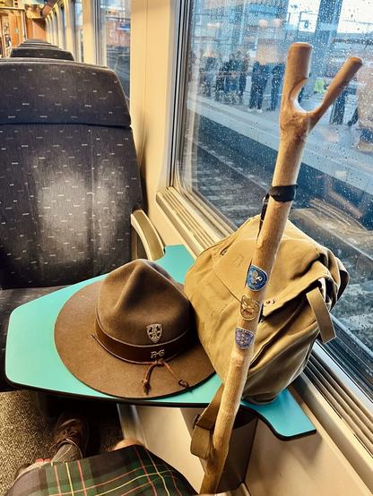 On the train, on my way to Ypres.
A table in a train, a scout had and a green bag on it, and a thumbstick leaning against it.