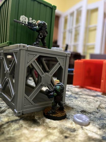 A Palanite Enforcer with a sniper rifle stands overwatch on a cargo container while a Palanite Enforcer with an enforcer boltgun advances below