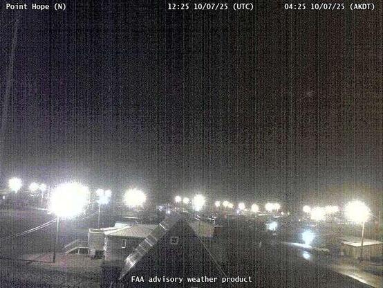 A webcam overseeing a beach with an ocean view, with a few small buildings and utility poles.