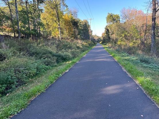 Photo looking up a smooth rail-trail with clear skies but shady because it's late afternoon.