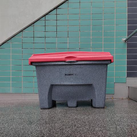 A grey box with red lid in front of a tiled wall