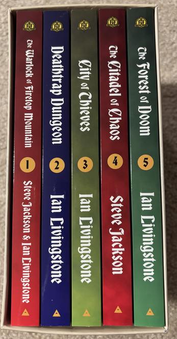 The spines of five Fighting Fantasy game books in a slipcase. The titles are The Warlock of Firetop Mountain, Deathtrap Dungeon, City of Thieves, The Citadel of Chaos, and The Forest of Doom.