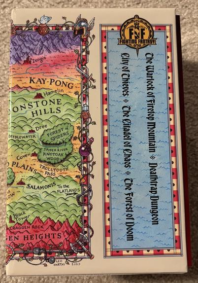 The front of the Fighting Fantasy slipcase. The left side shows a colorful world map, the right side lists the included books’ titles.