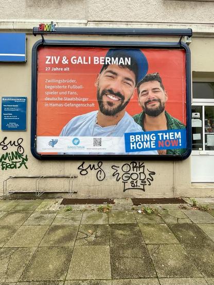 Eine große Plakatwand an einem Haus mit Fußweg davor. Darauf ein Plakat mit folgendem Text:“ZIV & GALI BERMAN 27 Jahre alt Zwillingsbrüder, begeisterte Fußballspieler und Fans, deutsche Staatsbürger in Hamas-Gefangenschaft JUNGES FORUM BRING THEM HOME NOW!“ Dazu ein Foto der beiden. Beide aind bärtig und und in sommerlicher Kleidung. Sie sind in guter Stimmung und lächeln.