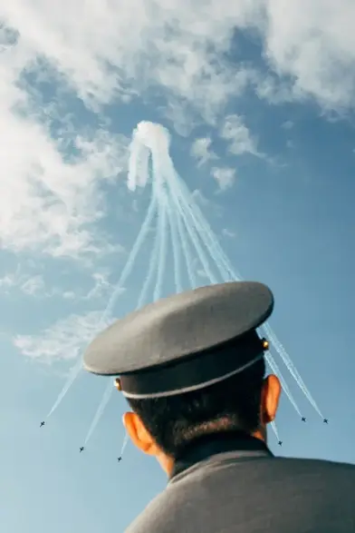 Ein von hinten gesehener Mensch in Militäruniform sieht zum Himmel auf, bei dem Kampfflugzeuge Flugkunststückchen machen.