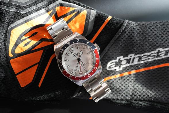 An opaline dial Tudor Black Bay GMT on top of a black and orange alpinestars racing glove.