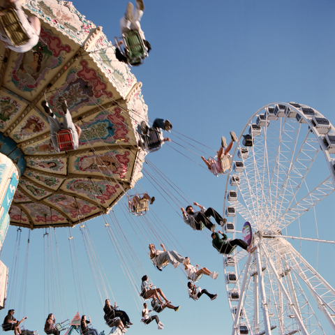 The old fashioned carnival swing and ferris wheel split the frame with an arc of swingers between.
