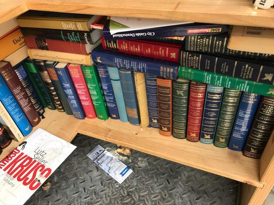 Foto aus einem öffentlichen Bücherschrank. Viele Readers Digest Bücher, überfüllt, am Boden liegt ein Lesezeichen.