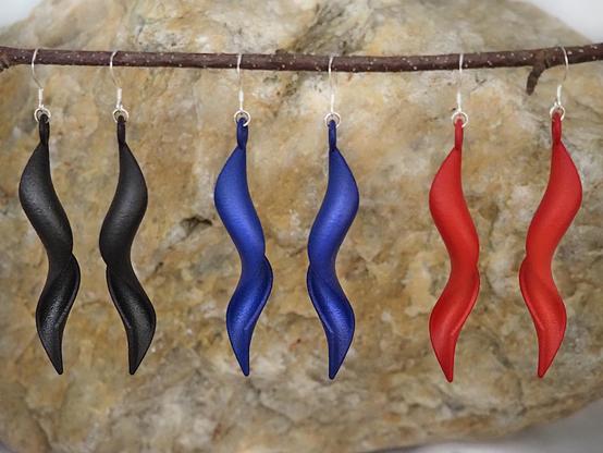 A photograph of three pairs of undulating nylon earrings, in black, blue, and red.