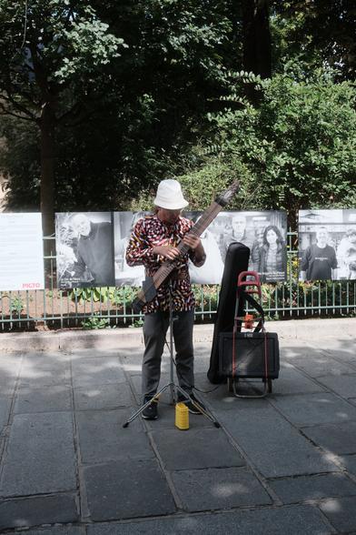 A man busking on the street on an string instrument made of a single block of wood, with a pickup, linked to an amp
