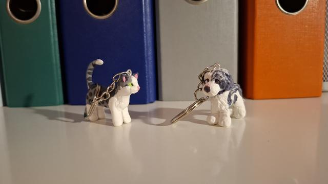 Two foam clay keychains, one of a grey tabby and white cat, and the other of a grey and white sheepdog.