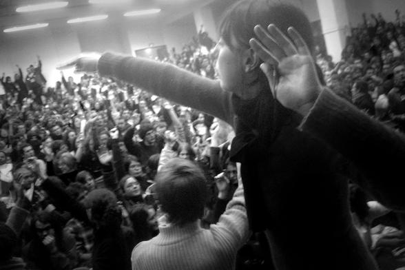 Photo en noir et blanc d'une assemblée générale pendant le mouvement contre la loi contrat premiere embauche à Paris en 2006. On voit une étudiante au premier rang qui semble compter les voix dans l'assemblée