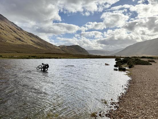 Cyclist holding bike above head up to waist in river.