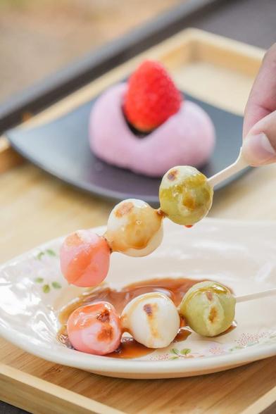 Dango skewers with pink, white, and green mochi drizzled with sauce, plus a mochi with a strawberry on a plate.