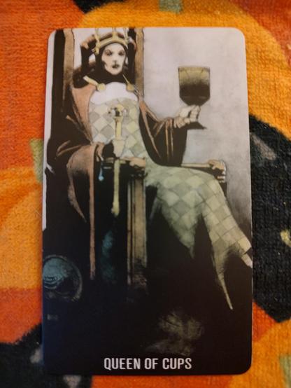 Card from the Joker Tarot deck. 
Queen of Cups.
A woman on a throne, wearing a checkered dress, holds a scepter and a large chalice in her hands.